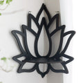 A black wooden wall shelf shaped like a lotus flower, mounted in the corner of a room. The shelf holds a candle in a glass holder, several crystal stones, and a small spray bottle. Decorative and compact, it adds a serene, spiritual touch to the space. Dimensions are 23cm (9.05in) wide and 29cm (11.41in) tall.