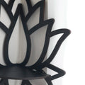 A black wooden wall shelf shaped like a lotus flower, mounted in the corner of a room. The shelf holds a candle in a glass holder, several crystal stones, and a small spray bottle. Decorative and compact, it adds a serene, spiritual touch to the space. Dimensions are 23cm (9.05in) wide and 29cm (11.41in) tall.