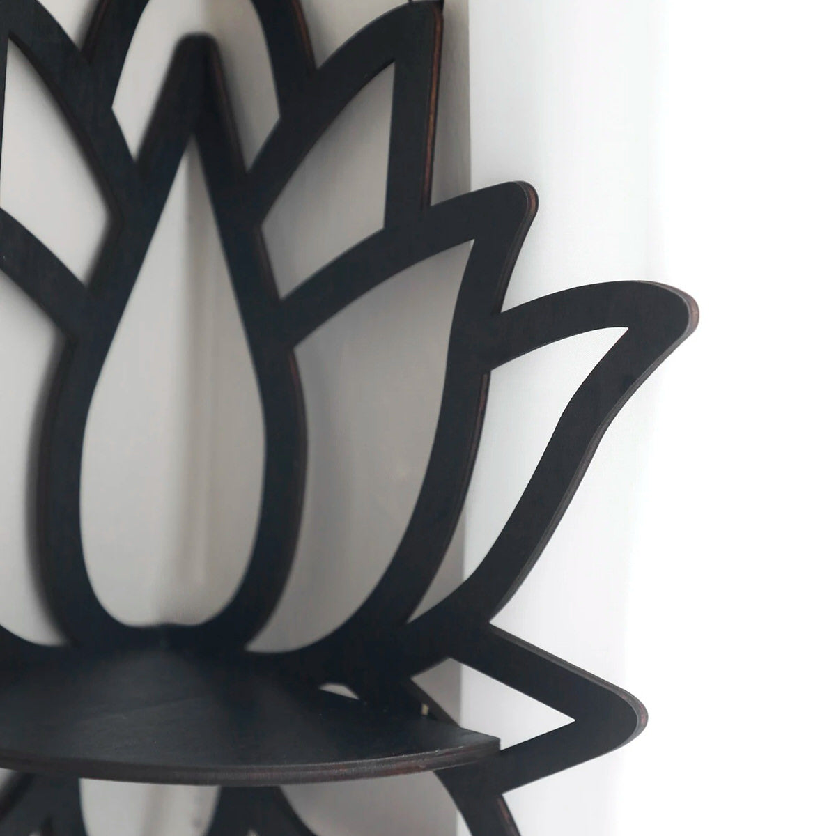 A black wooden wall shelf shaped like a lotus flower, mounted in the corner of a room. The shelf holds a candle in a glass holder, several crystal stones, and a small spray bottle. Decorative and compact, it adds a serene, spiritual touch to the space. Dimensions are 23cm (9.05in) wide and 29cm (11.41in) tall.