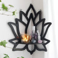 A black wooden wall shelf shaped like a lotus flower, mounted in the corner of a room. The shelf holds a candle in a glass holder, several crystal stones, and a small spray bottle. Decorative and compact, it adds a serene, spiritual touch to the space. Dimensions are 23cm (9.05in) wide and 29cm (11.41in) tall.