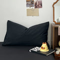 Creamy white bedding set printed with black outlined floral designs, giving a delicate and minimalist look. The bedding is soft and rumpled, styled with black pillows and cozy bedroom decor.