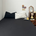 Creamy white bedding set printed with black outlined floral designs, giving a delicate and minimalist look. The bedding is soft and rumpled, styled with black pillows and cozy bedroom decor.