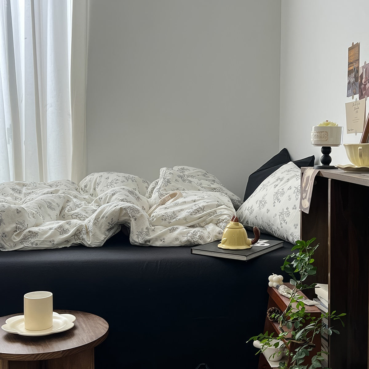 Creamy white bedding set printed with black outlined floral designs, giving a delicate and minimalist look. The bedding is soft and rumpled, styled with black pillows and cozy bedroom decor.