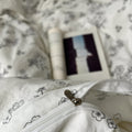 Creamy white bedding set printed with black outlined floral designs, giving a delicate and minimalist look. The bedding is soft and rumpled, styled with black pillows and cozy bedroom decor.