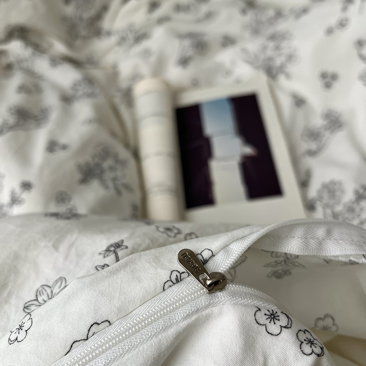 Creamy white bedding set printed with black outlined floral designs, giving a delicate and minimalist look. The bedding is soft and rumpled, styled with black pillows and cozy bedroom decor.