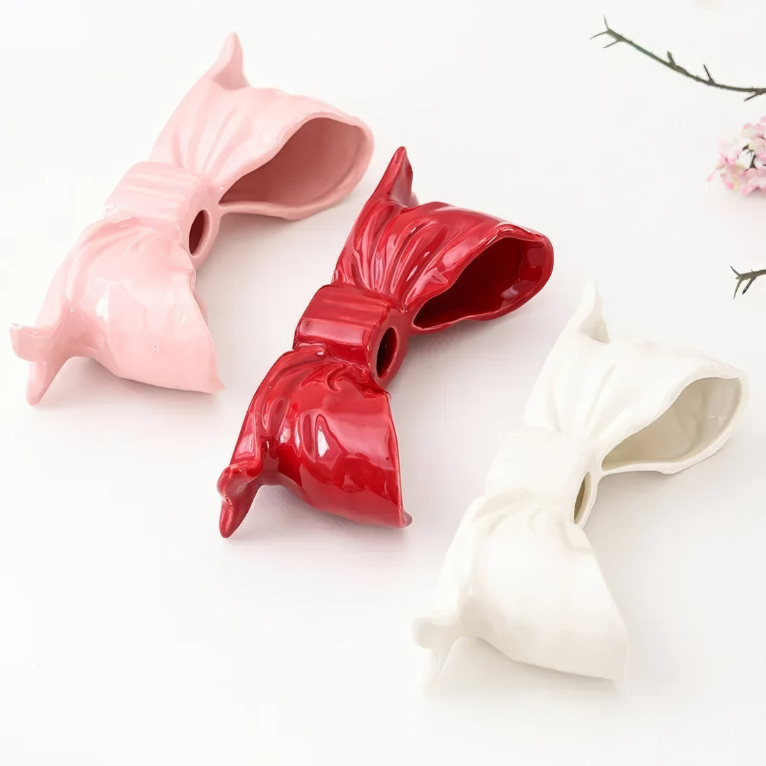 Ceramic bow-shaped candle holder in pink, red, and white with a glossy finish, designed to hold taper candles; decorative and elegant for home decor.