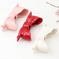 Ceramic bow-shaped candle holder in pink, red, and white with a glossy finish, designed to hold taper candles; decorative and elegant for home decor.