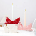 Ceramic bow-shaped candle holder in pink, red, and white with a glossy finish, designed to hold taper candles; decorative and elegant for home decor.