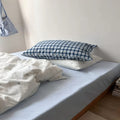 Bed with checkered pillow and white bedding against a plain wall