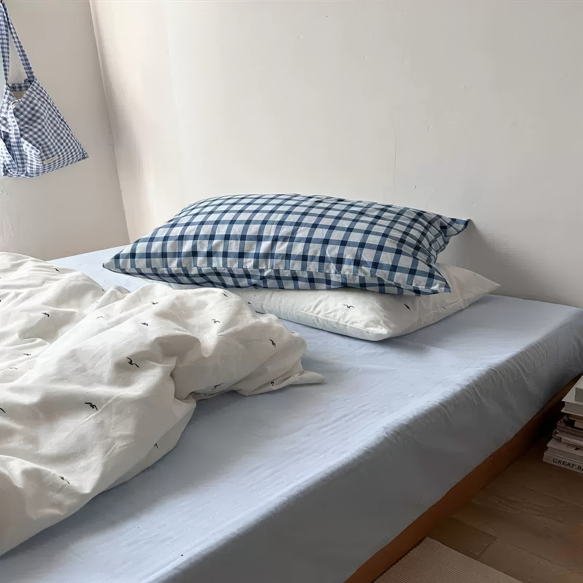 Bed with checkered pillow and white bedding against a plain wall