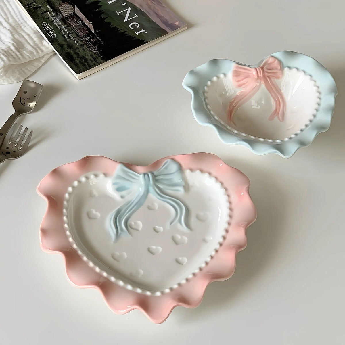 A pastel-colored, heart-shaped ceramic plate featuring scalloped edges, embossed hearts, and an elegant bow accent. Available in soft pink, pastel blue, and delicate yellow colors.