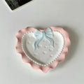 A pastel-colored, heart-shaped ceramic plate featuring scalloped edges, embossed hearts, and an elegant bow accent. Available in soft pink, pastel blue, and delicate yellow colors.