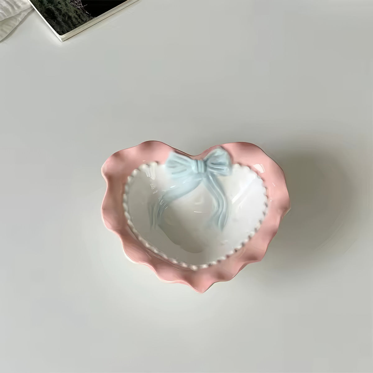 A pastel-colored, heart-shaped ceramic plate featuring scalloped edges, embossed hearts, and an elegant bow accent. Available in soft pink, pastel blue, and delicate yellow colors.