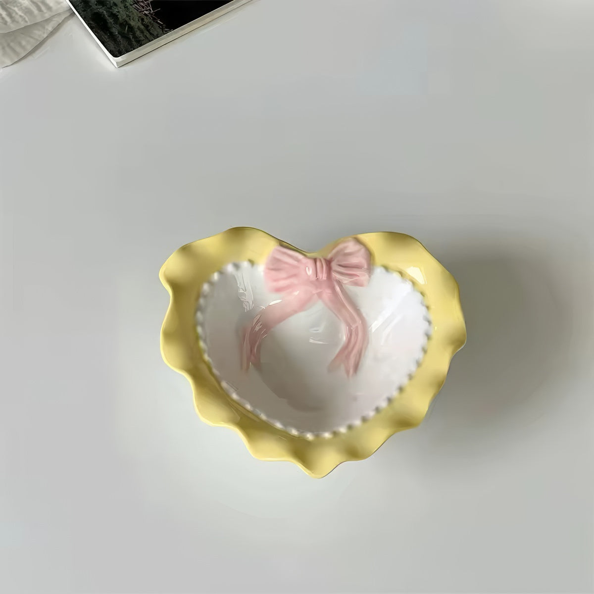 A pastel-colored, heart-shaped ceramic plate featuring scalloped edges, embossed hearts, and an elegant bow accent. Available in soft pink, pastel blue, and delicate yellow colors.