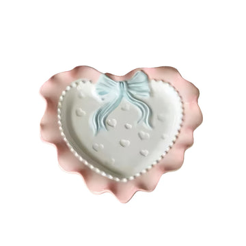 A pastel-colored, heart-shaped ceramic plate featuring scalloped edges, embossed hearts, and an elegant bow accent. Available in soft pink, pastel blue, and delicate yellow colors.
