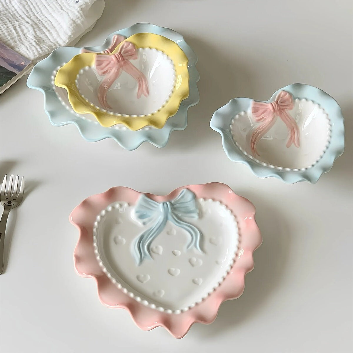 A pastel-colored, heart-shaped ceramic plate featuring scalloped edges, embossed hearts, and an elegant bow accent. Available in soft pink, pastel blue, and delicate yellow colors.