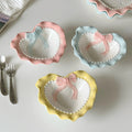A pastel-colored, heart-shaped ceramic plate featuring scalloped edges, embossed hearts, and an elegant bow accent. Available in soft pink, pastel blue, and delicate yellow colors.
