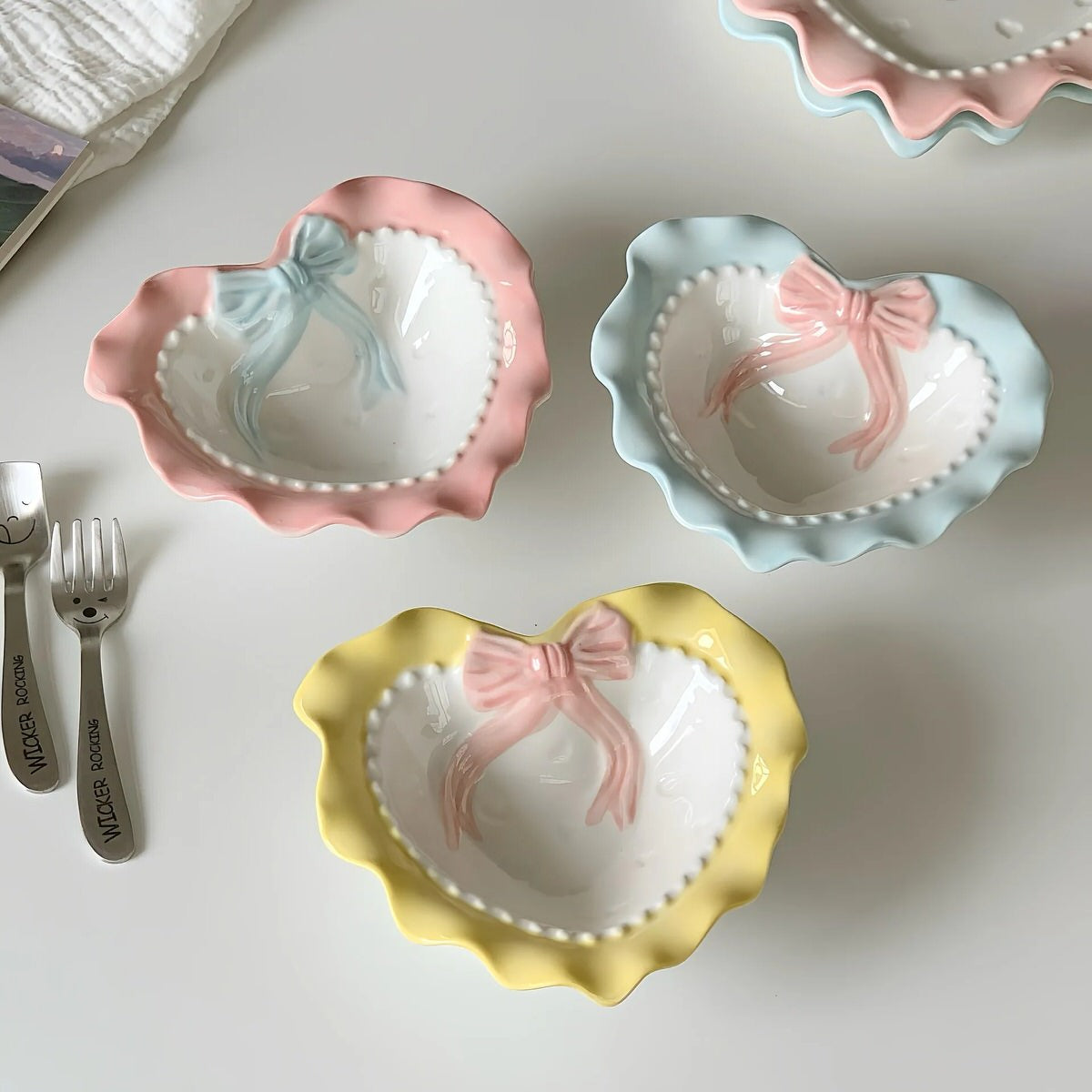 A pastel-colored, heart-shaped ceramic plate featuring scalloped edges, embossed hearts, and an elegant bow accent. Available in soft pink, pastel blue, and delicate yellow colors.