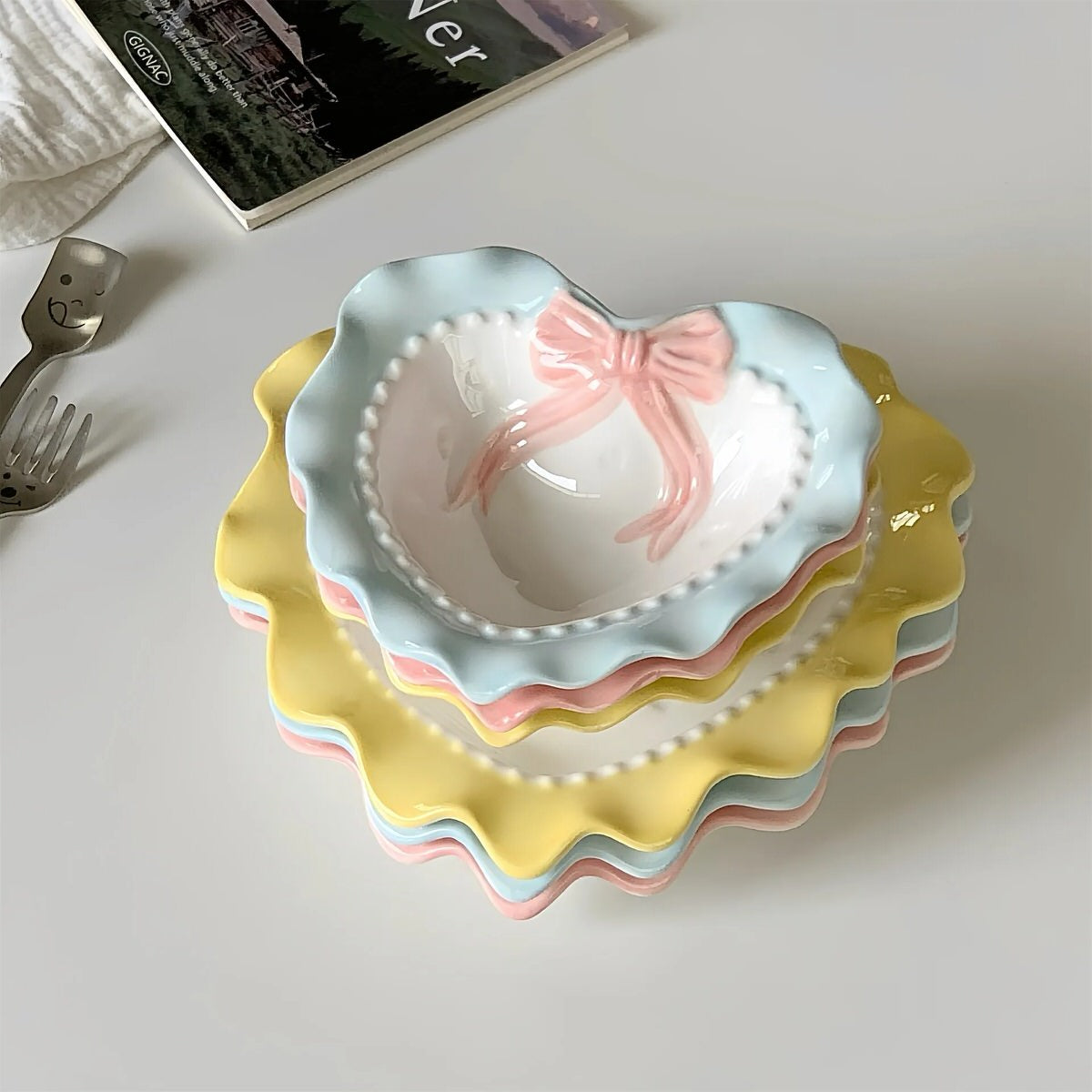 A pastel-colored, heart-shaped ceramic plate featuring scalloped edges, embossed hearts, and an elegant bow accent. Available in soft pink, pastel blue, and delicate yellow colors.