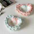 A pastel-colored, heart-shaped ceramic plate featuring scalloped edges, embossed hearts, and an elegant bow accent. Available in soft pink, pastel blue, and delicate yellow colors.