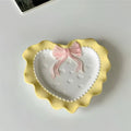 A pastel-colored, heart-shaped ceramic plate featuring scalloped edges, embossed hearts, and an elegant bow accent. Available in soft pink, pastel blue, and delicate yellow colors.