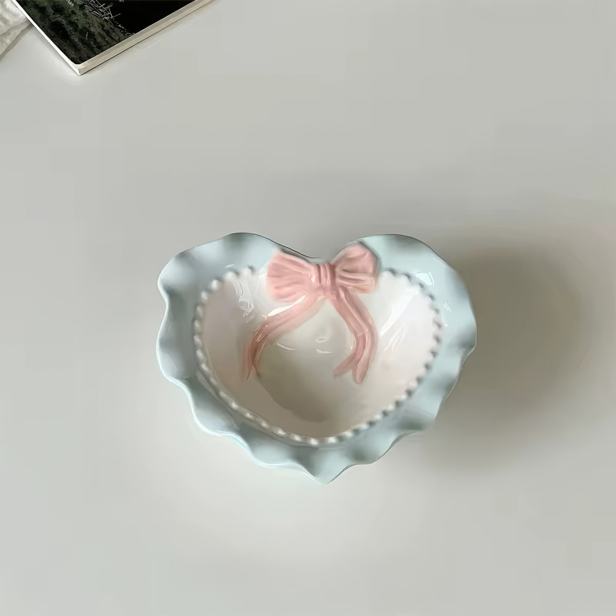 A pastel-colored, heart-shaped ceramic plate featuring scalloped edges, embossed hearts, and an elegant bow accent. Available in soft pink, pastel blue, and delicate yellow colors.