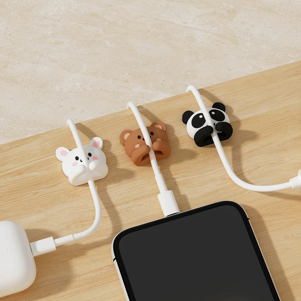 Set of two black-and-white kawaii panda cable organizer clips made of silicone, holding charging cables neatly