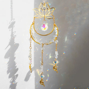 A golden suncatcher featuring a lotus flower at the top, a crescent-shaped ring adorned with white crystal chips, and a central hanging prism. Three crystal and charm strands dangle below, reflecting rainbow light patterns onto the surrounding wall. The full hanging length is 44cm (17.32in).