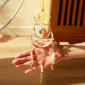 A golden suncatcher featuring a lotus flower at the top, a crescent-shaped ring adorned with white crystal chips, and a central hanging prism. Three crystal and charm strands dangle below, reflecting rainbow light patterns onto the surrounding wall. The full hanging length is 44cm (17.32in).