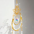 A golden suncatcher featuring a lotus flower at the top, a crescent-shaped ring adorned with white crystal chips, and a central hanging prism. Three crystal and charm strands dangle below, reflecting rainbow light patterns onto the surrounding wall. The full hanging length is 44cm (17.32in).