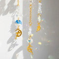 A golden suncatcher featuring a lotus flower at the top, a crescent-shaped ring adorned with white crystal chips, and a central hanging prism. Three crystal and charm strands dangle below, reflecting rainbow light patterns onto the surrounding wall. The full hanging length is 44cm (17.32in).