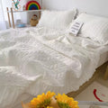 White quilted comforter on a bed with pillows and sunflowers in the foreground.