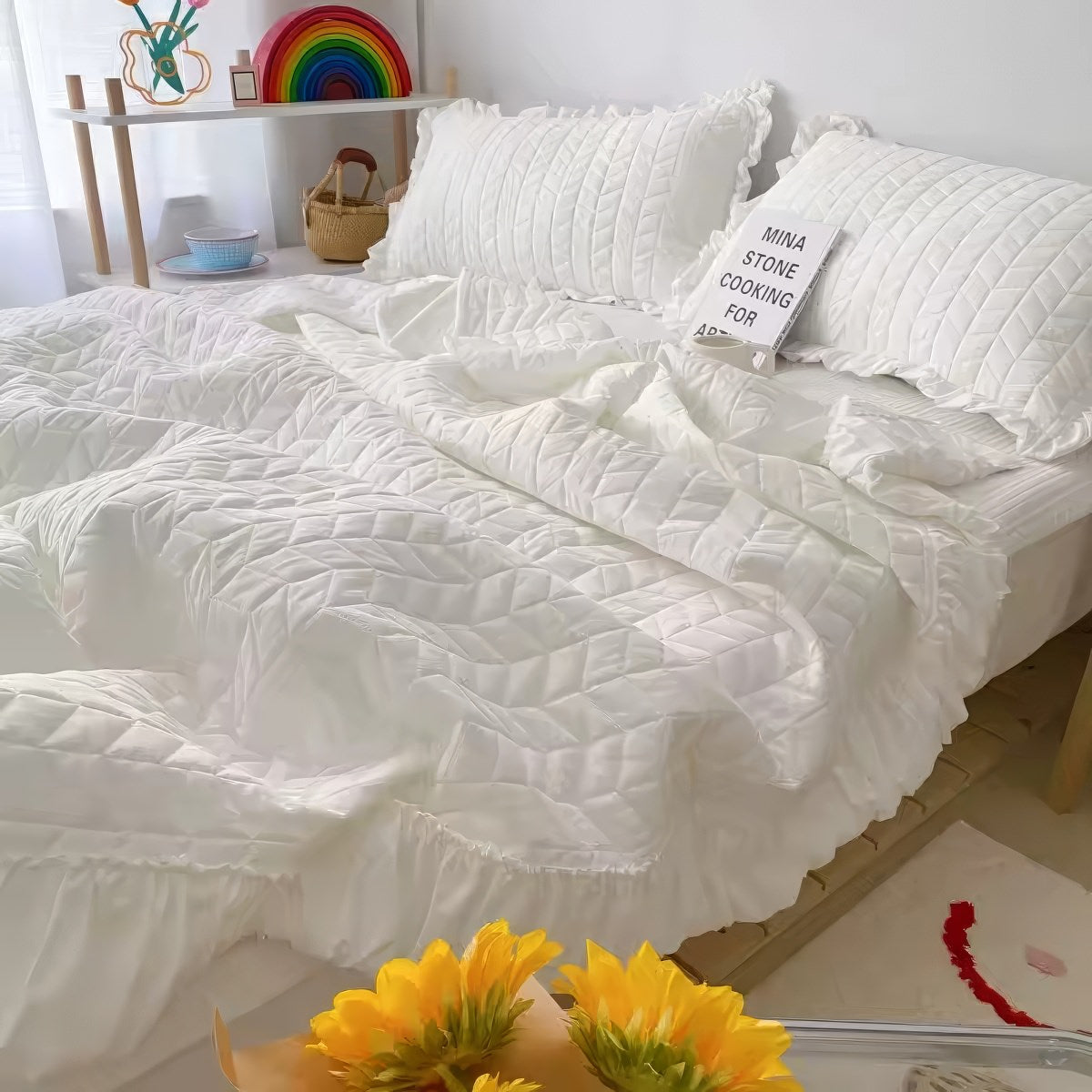 White quilted comforter on a bed with pillows and sunflowers in the foreground.