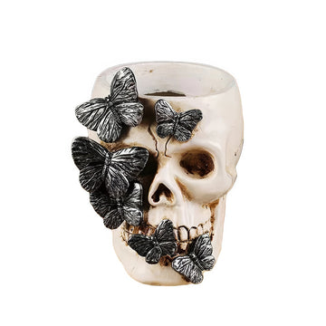 A resin brush holder designed as a skull decorated with detailed black butterflies. It measures 8cm wide and 10.3cm tall