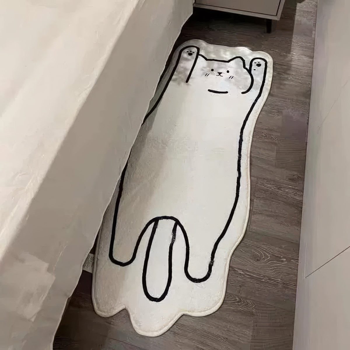 A soft, white floor mat shaped like a stretched-out cat with a simple black outline