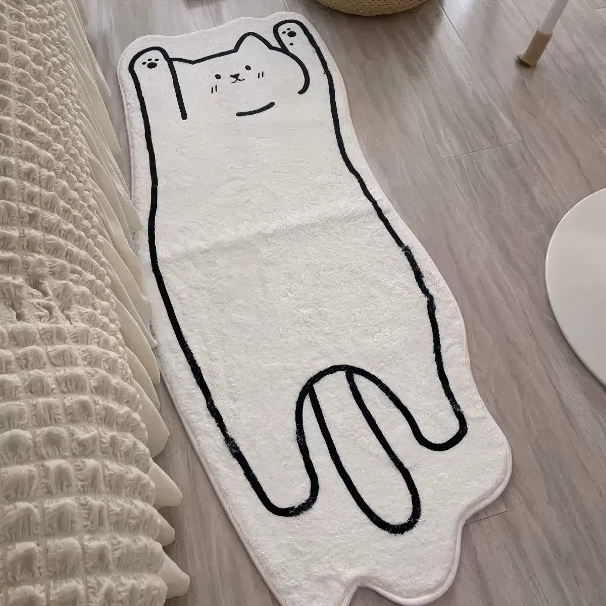 A soft, white floor mat shaped like a stretched-out cat with a simple black outline