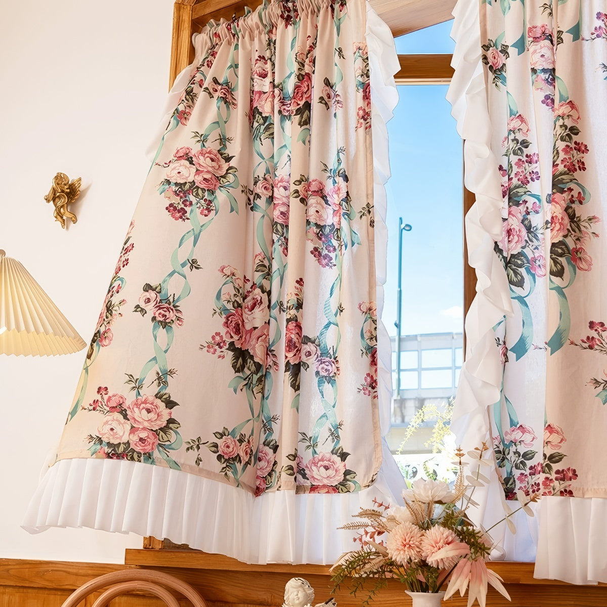 Floral curtains with a white ruffled trim in a room with a window and lamp.