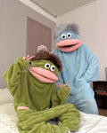 A green plush hooded one-piece pajama or costume with a frog-like face, large white eyes, a pink mouth, and a small matching frog patch on the chest