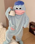A green plush hooded one-piece pajama or costume with a frog-like face, large white eyes, a pink mouth, and a small matching frog patch on the chest