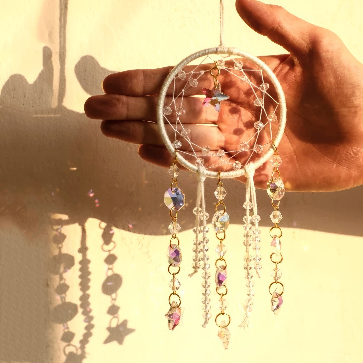 Crystal dreamcatcher wall hanging with prism beads, star charms, and sun-catching crystal strands in ivory and pink designs.