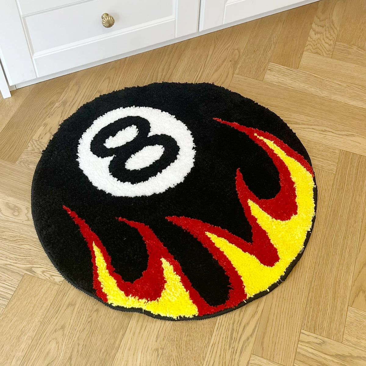 Round tufted rug with a black eight-ball design and red-yellow flame pattern.
