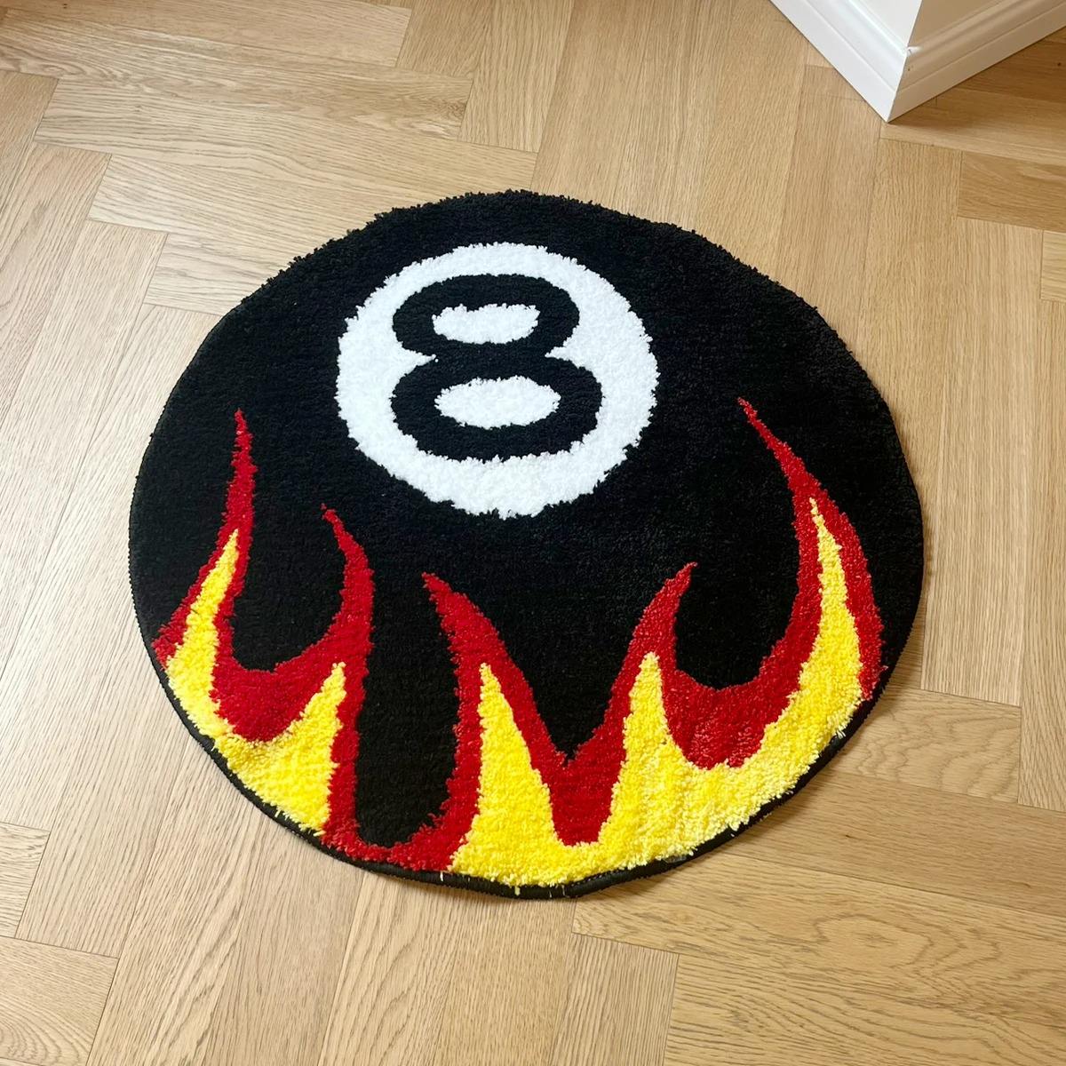 Round tufted rug with a black eight-ball design and red-yellow flame pattern.