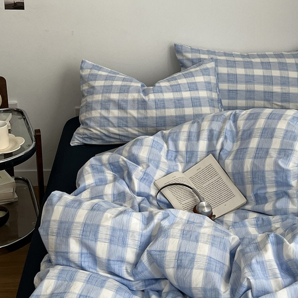 Minimalist bedroom with soft blue and white gingham duvet cover set and matching pillowcases on a dark fitted sheet.