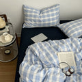 Minimalist bedroom with soft blue and white gingham duvet cover set and matching pillowcases on a dark fitted sheet.
