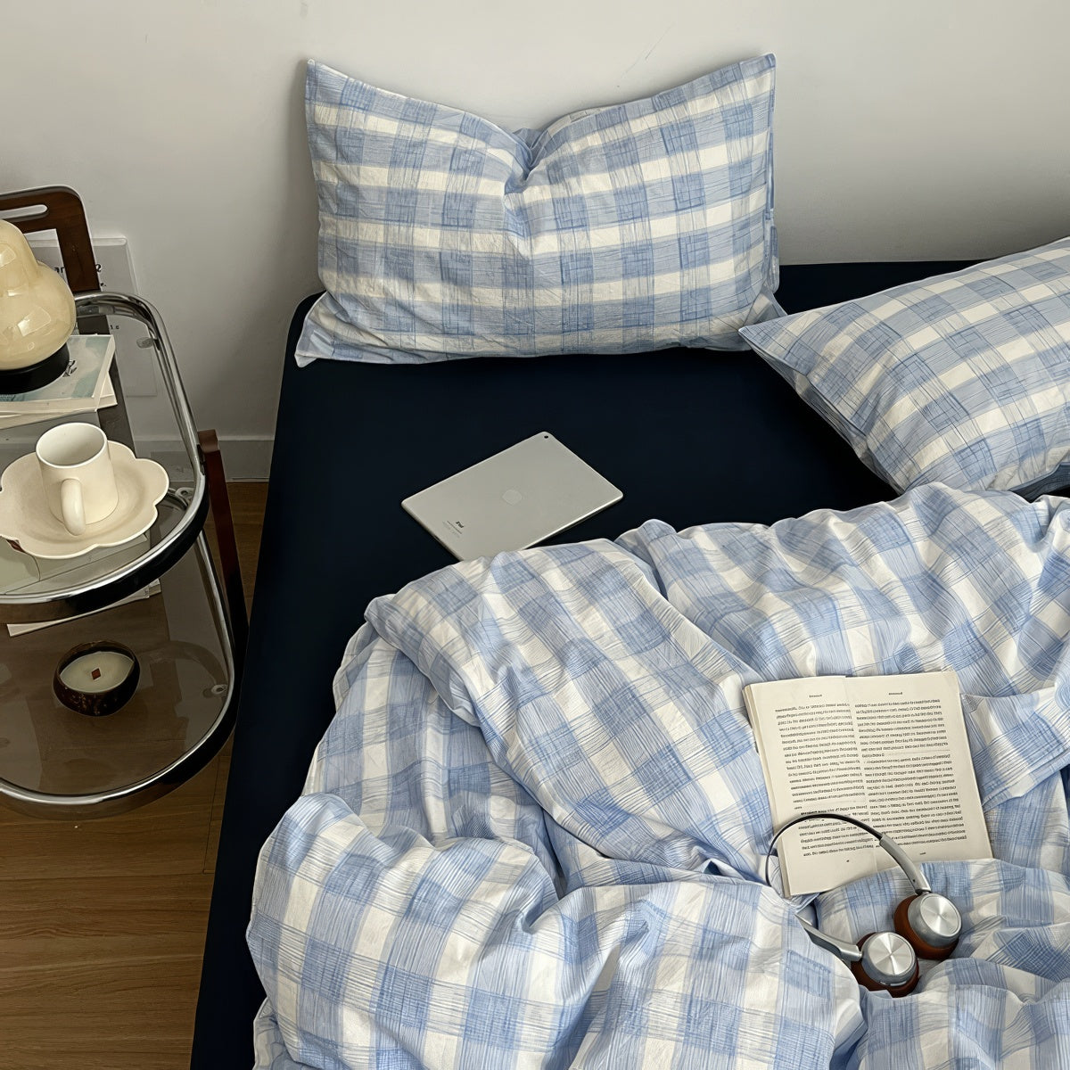 Minimalist bedroom with soft blue and white gingham duvet cover set and matching pillowcases on a dark fitted sheet.