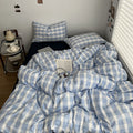 Minimalist bedroom with soft blue and white gingham duvet cover set and matching pillowcases on a dark fitted sheet.