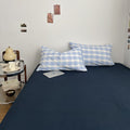 Minimalist bedroom with soft blue and white gingham duvet cover set and matching pillowcases on a dark fitted sheet.