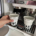 White ceramic coffee mug shaped like a crumpled takeaway coffee cup with black TOASTING lettering and #coffee print around the rim.