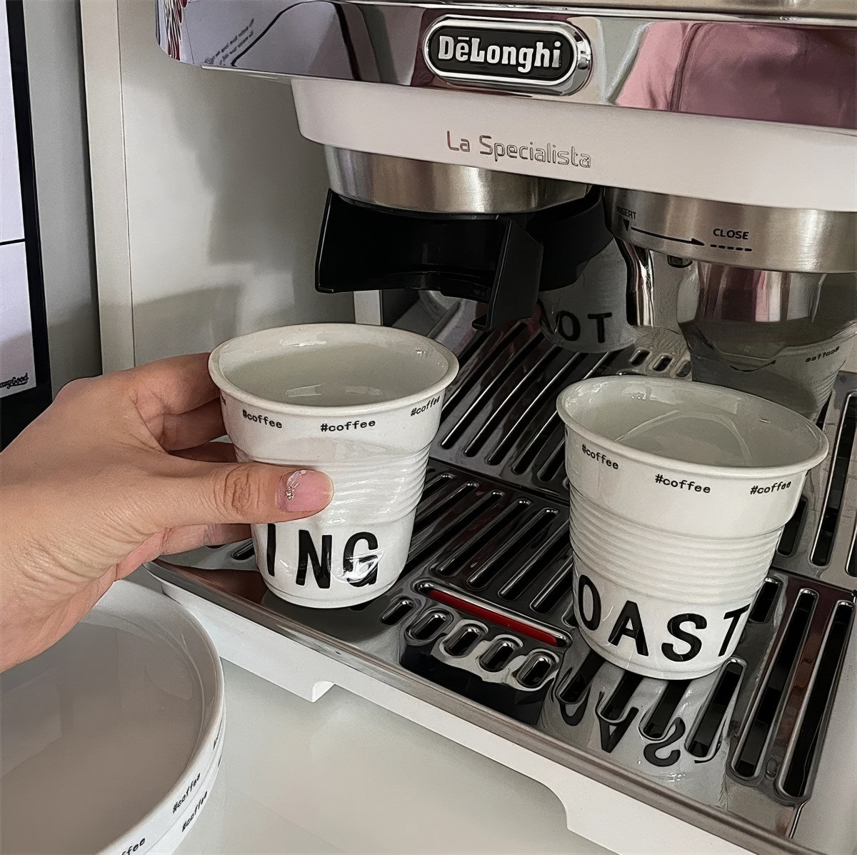 White ceramic coffee mug shaped like a crumpled takeaway coffee cup with black TOASTING lettering and #coffee print around the rim.