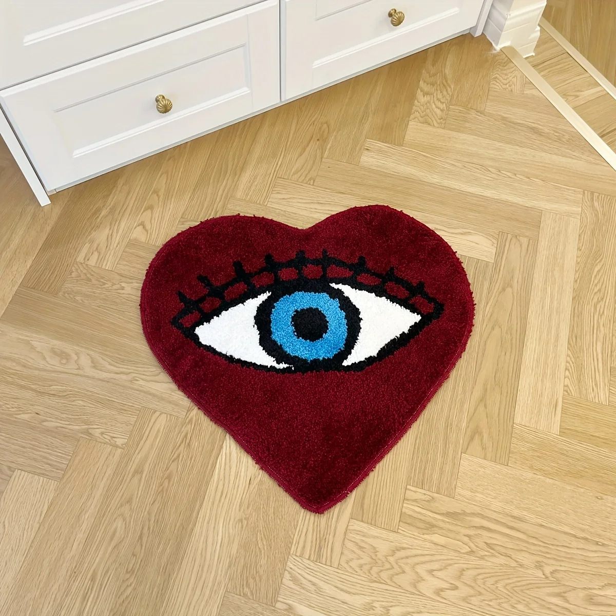 Heart-shaped dark red tufted rug with a large blue evil eye design and black lashes